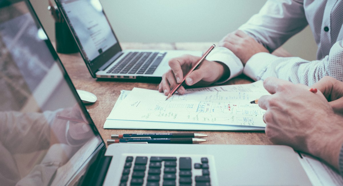 Proofreading ve editing farkını değerlendiren editörler dizüstü bilgisayar başında basılı metin üzerinde çalışırken